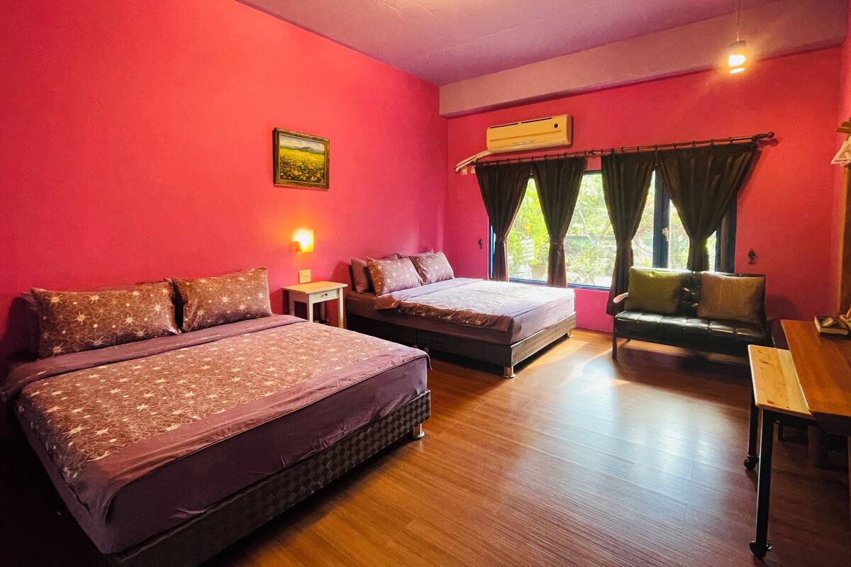 A room with two beds, a sofa, a table, and an air conditioning unit.