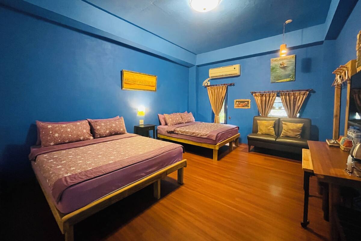 A room with two beds, a sofa, a table, and a ceiling light.