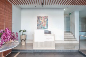 A reception area with a wooden reception desk, a potted plant, and a colorful abstract painting on the wall. - OYO Flagship 755 Appartel Grand Dhika City (Bekasi)