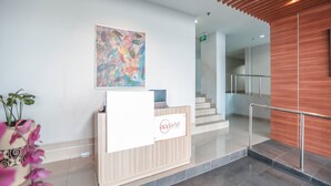 A modern reception desk with a logo, a staircase, and a wall-mounted abstract painting. - OYO Flagship 755 Appartel Grand Dhika City (Bekasi)