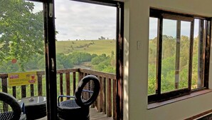 A wooden deck with a view of a green landscape. - Hills and Dales Accommodation (Lanseria)