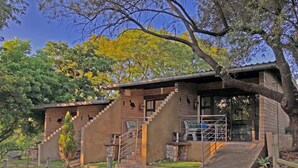A rustic building with a staircase leading to a door, surrounded by greenery and trees. - Hills and Dales Accommodation (Lanseria)