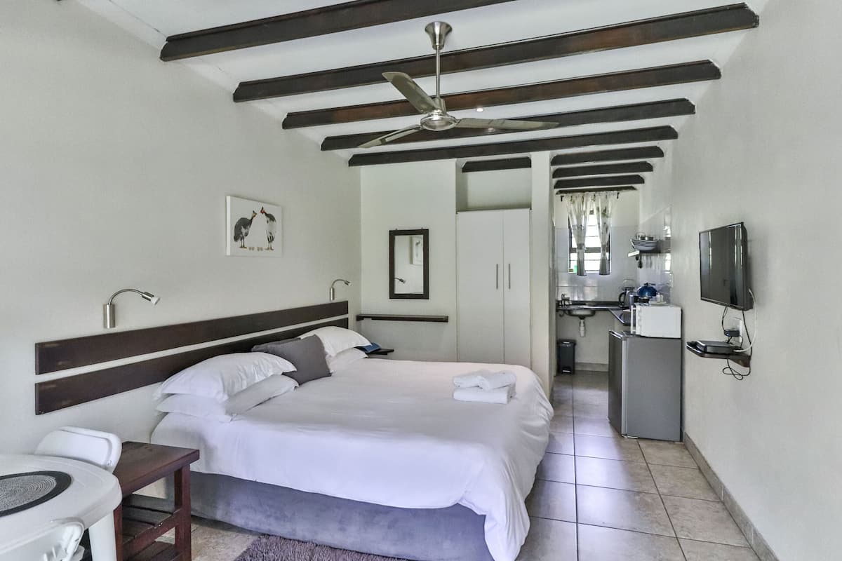 A hotel room with a bed, bedside table, ceiling fan, and a view into the kitchen area.