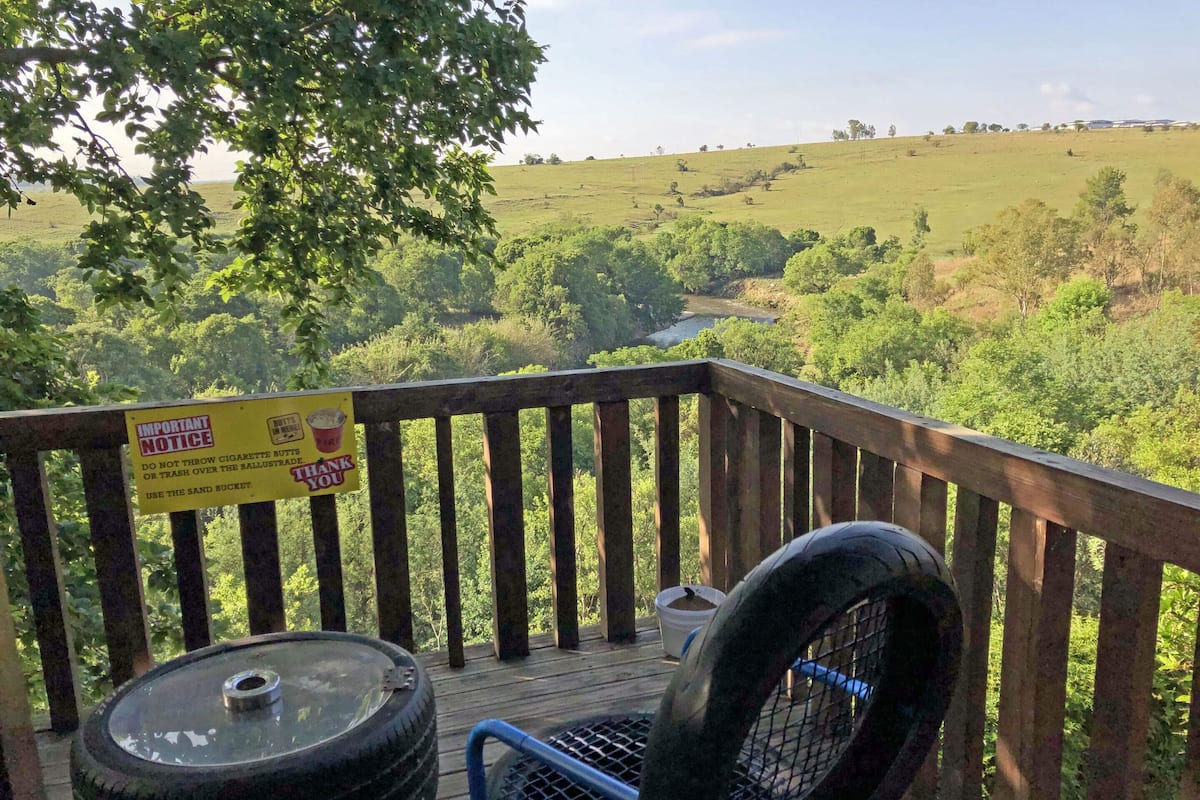 A wooden deck with a view of a green landscape, a sign about not throwing cigarette butts, and a tire grill.
