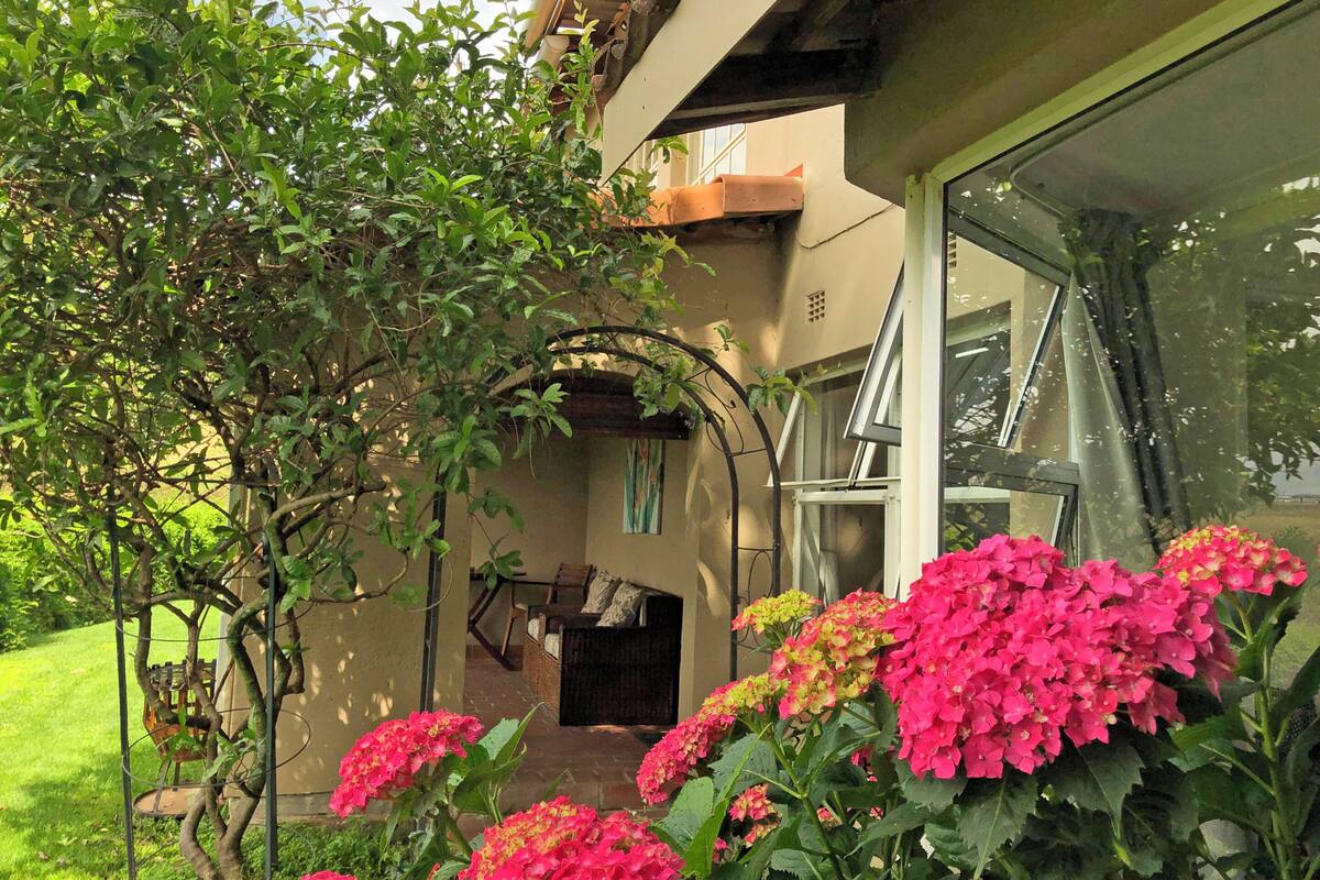 A garden with a pergola, a wooden bench, and a glass door leading to a covered patio area.