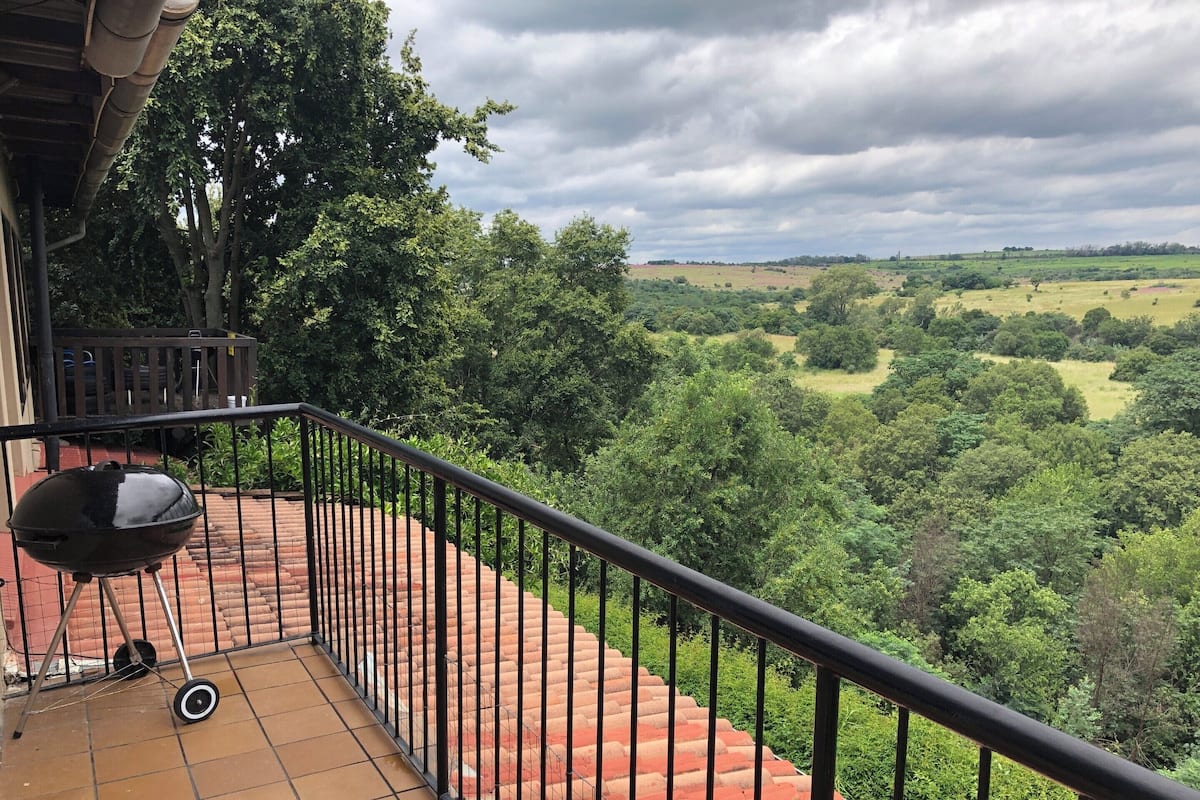 A balcony with a grill and a view of a green landscape.
