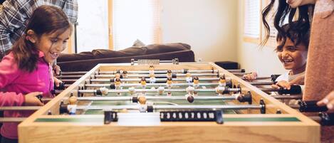 A foosball table in a room with a brown couch and a red wall decoration.