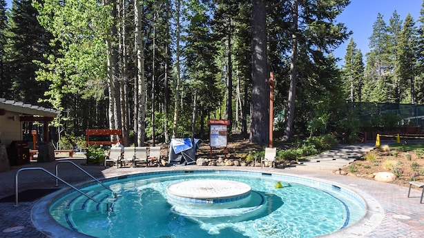 Un jacuzzi rond, entouré d’une terrasse en briques, avec une plateforme en bois et des chaises longues à l’arrière-plan.