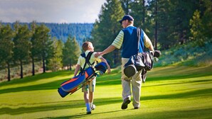Un homme et un enfant marchent sur un terrain de golf, portant des sacs de golf.