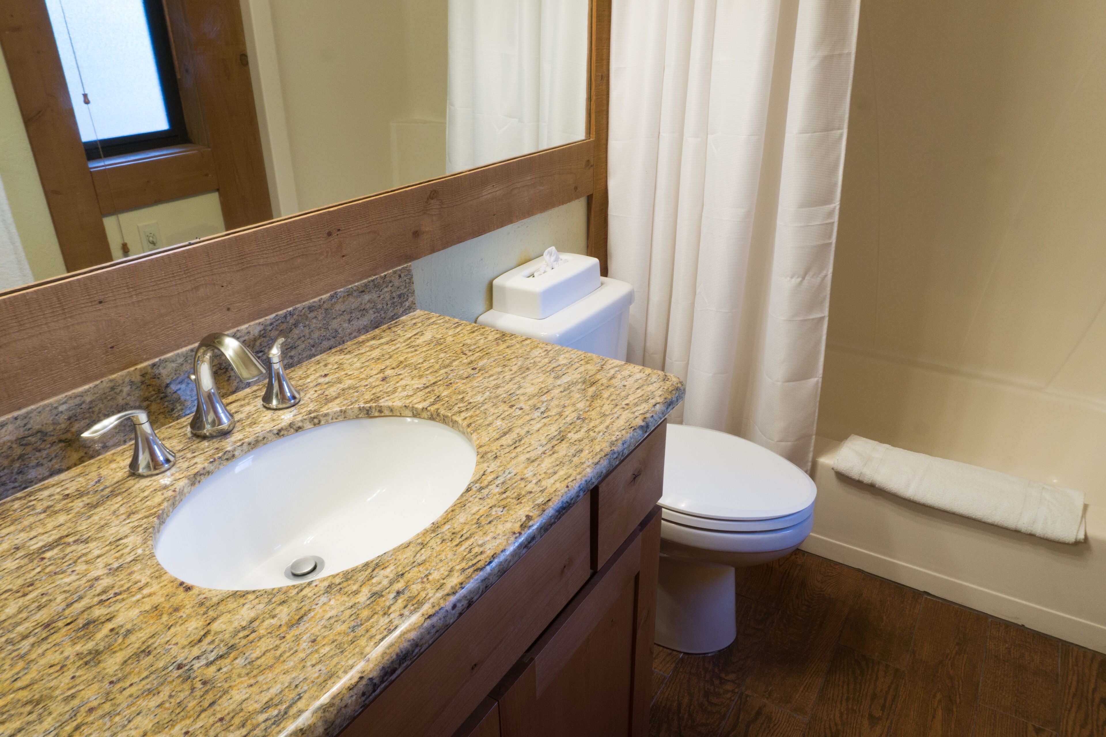 A bathroom with a granite countertop sink, a white toilet, a wooden cabinet, and a shower curtain.