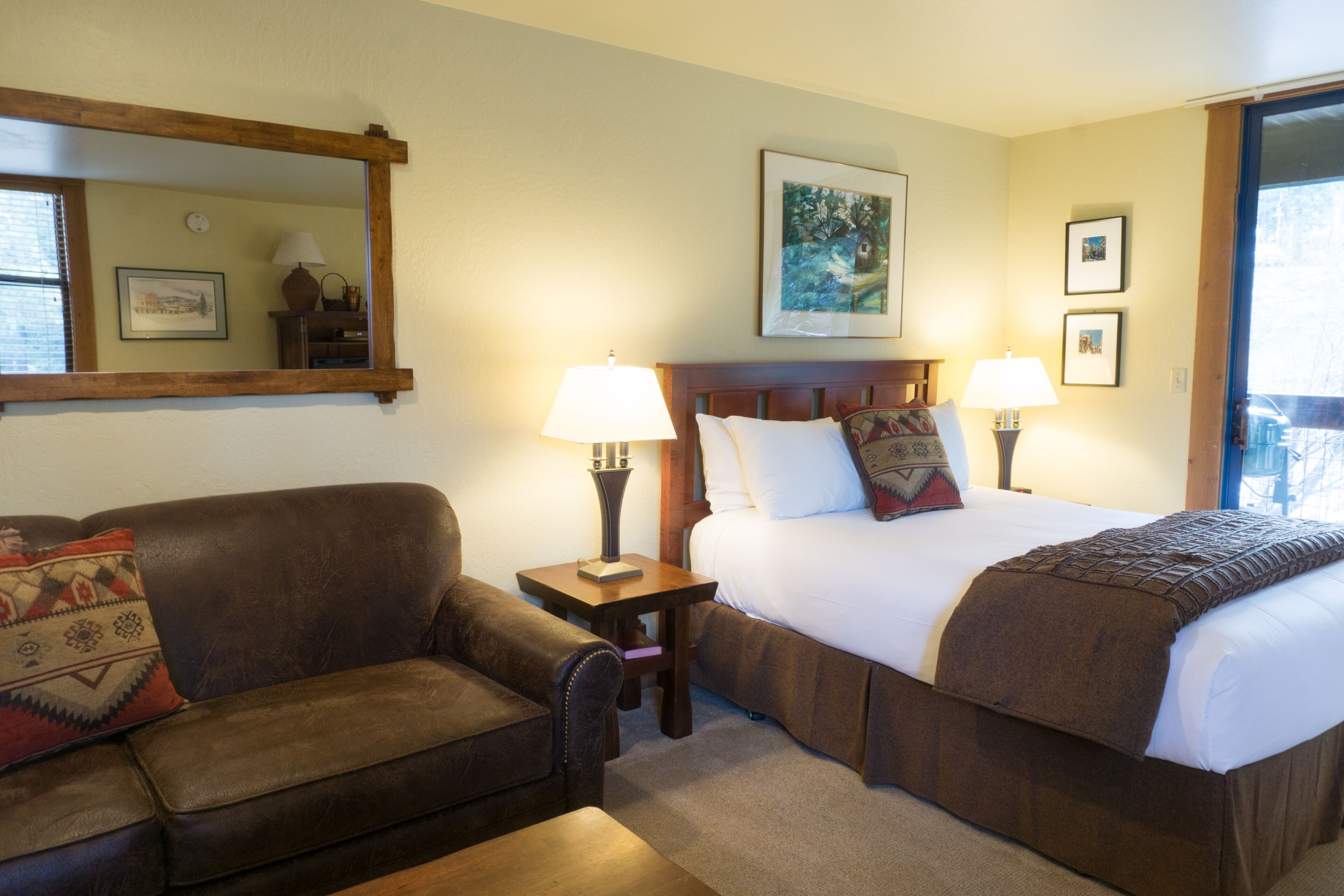 A hotel room with a bed, a sofa, a nightstand, a lamp, and a painting on the wall.