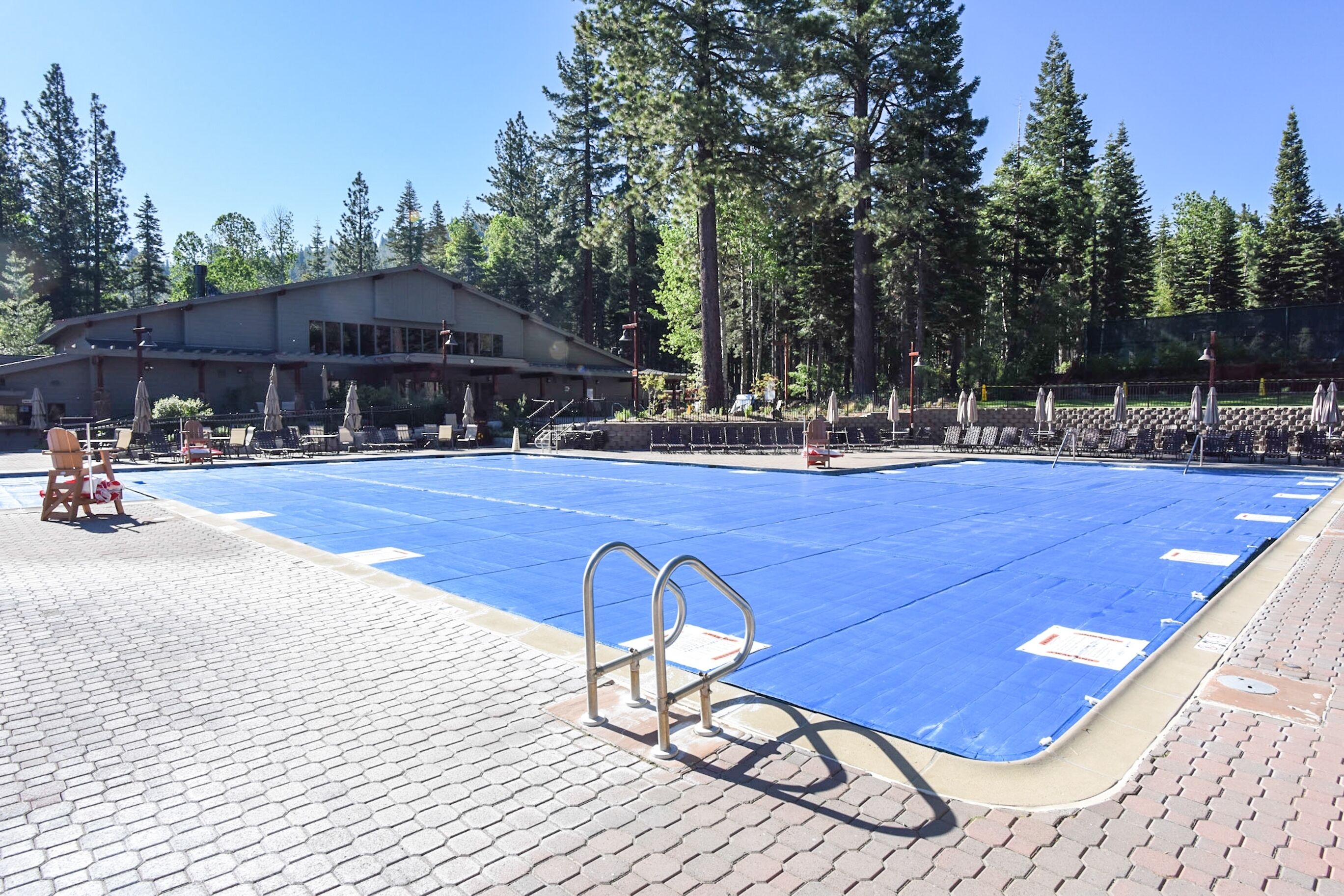 Une piscine avec un bord bleu, entourée de chaises longues et de parasols, et un bâtiment visible à l’arrière-plan.