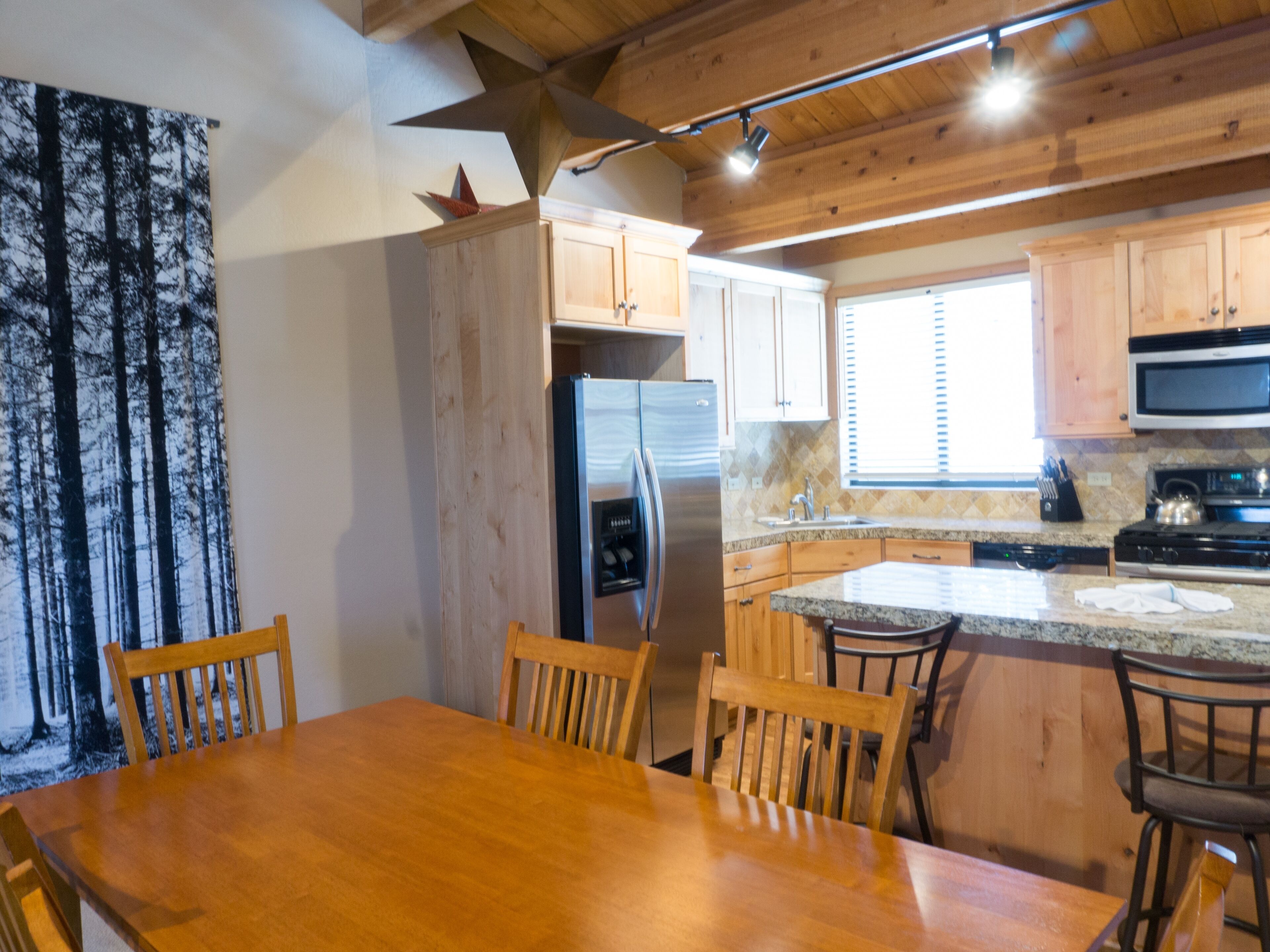A kitchen with wooden cabinets, a refrigerator, a microwave, and a stove. There is a dining table with chairs.