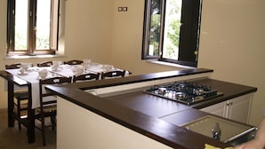A kitchen with a dining table set for four, a gas stove, and a window with a view of greenery. - B&B Mamma Elena (Rovito)