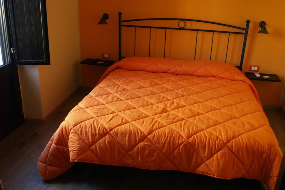 A bed with a quilted orange bedspread, two bedside tables with lamps, and a wooden floor.