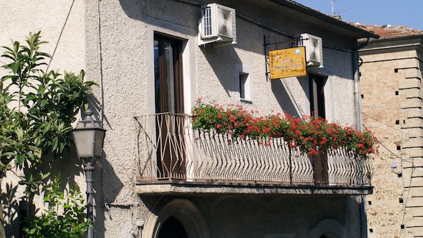 A building with a balcony featuring red flowers, a signboard, and an air conditioning unit. - B&B Mamma Elena (Rovito)