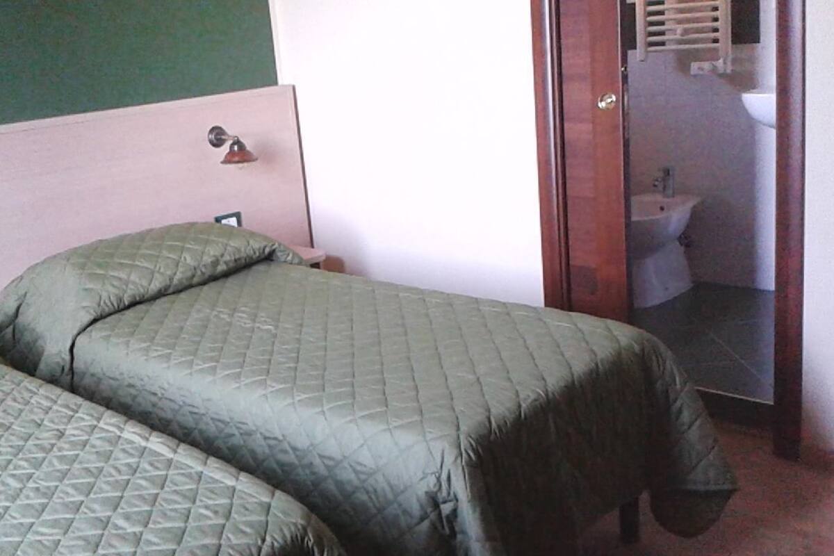 A room with two beds, a wooden headboard, a small bedside table, and a view of a bathroom through an open door.