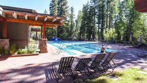 A swimming pool with lounge chairs and a covered area, surrounded by trees.