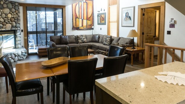 A cozy living room with a stone fireplace, a large sectional sofa, and a dining area with a wooden table and chairs.