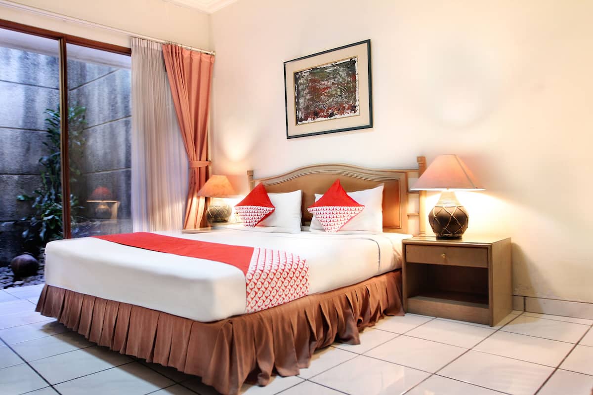 A neatly made bed with a red and white bedspread, two bedside lamps, and a framed picture on the wall.