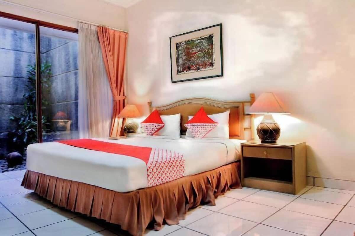 A hotel room with a bed, two bedside lamps, a nightstand, a window with curtains, and a painting on the wall.