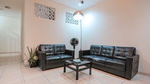 Ein Wohnzimmer mit zwei schwarzen Ledersofas, einem Glastisch, einer Stehlampe und dekorativen Wandverkleidungen.