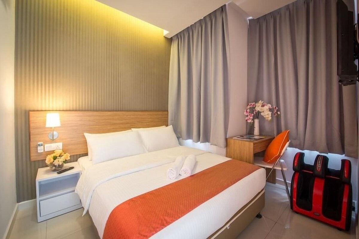 A hotel room with a bed, a nightstand with a lamp, a massage chair, and a wall-mounted TV.