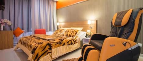 Habitación de hotel con cama, sillón de masajes, televisor y mesita de noche con lámpara.
