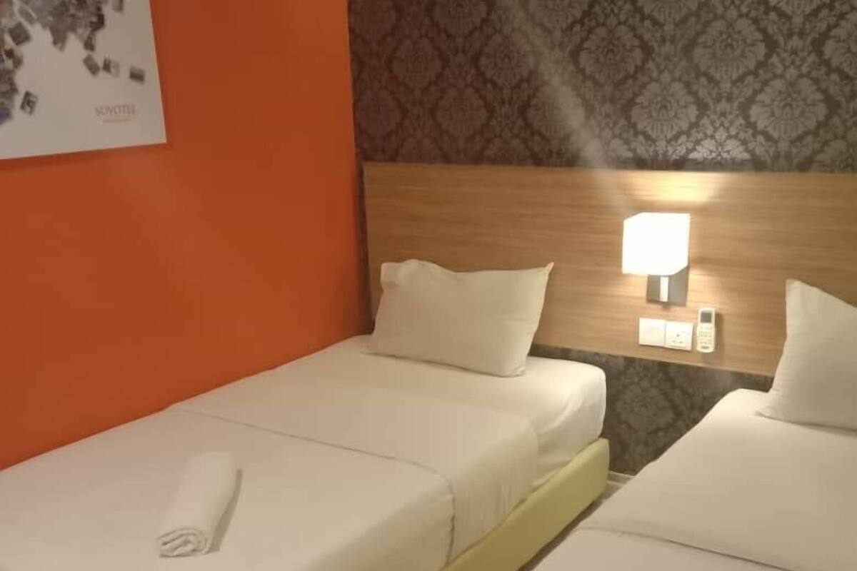 Una habitació d'hotel amb dos llits individuals, una tauleta de nit amb una làmpada i un paper pintat amb motius al mur.