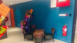 A hotel lobby with a blue wall, a reception desk, a fire extinguisher, and a small table with chairs. - Sovotel 9 Puchong (Puchong)