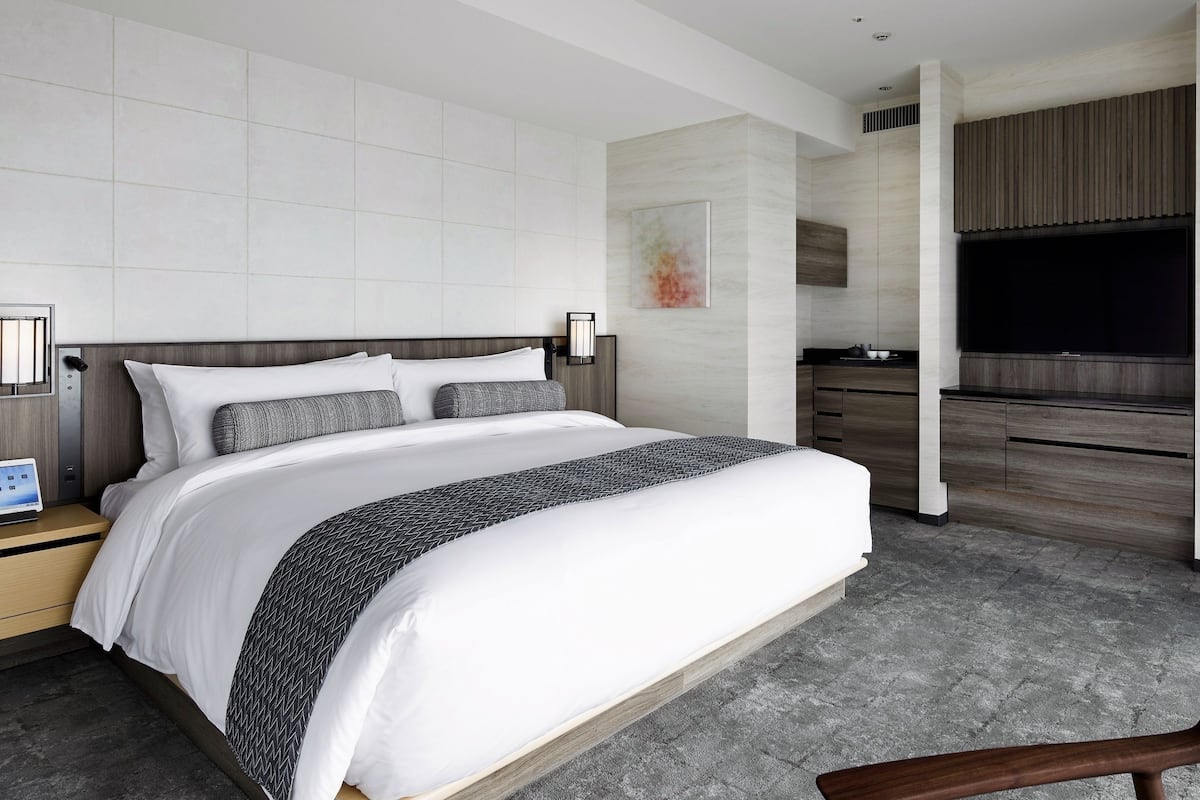 Habitación de hotel moderna con una cama grande, un escritorio con una computadora portátil, un televisor de pantalla plana y vistas a la ciudad.