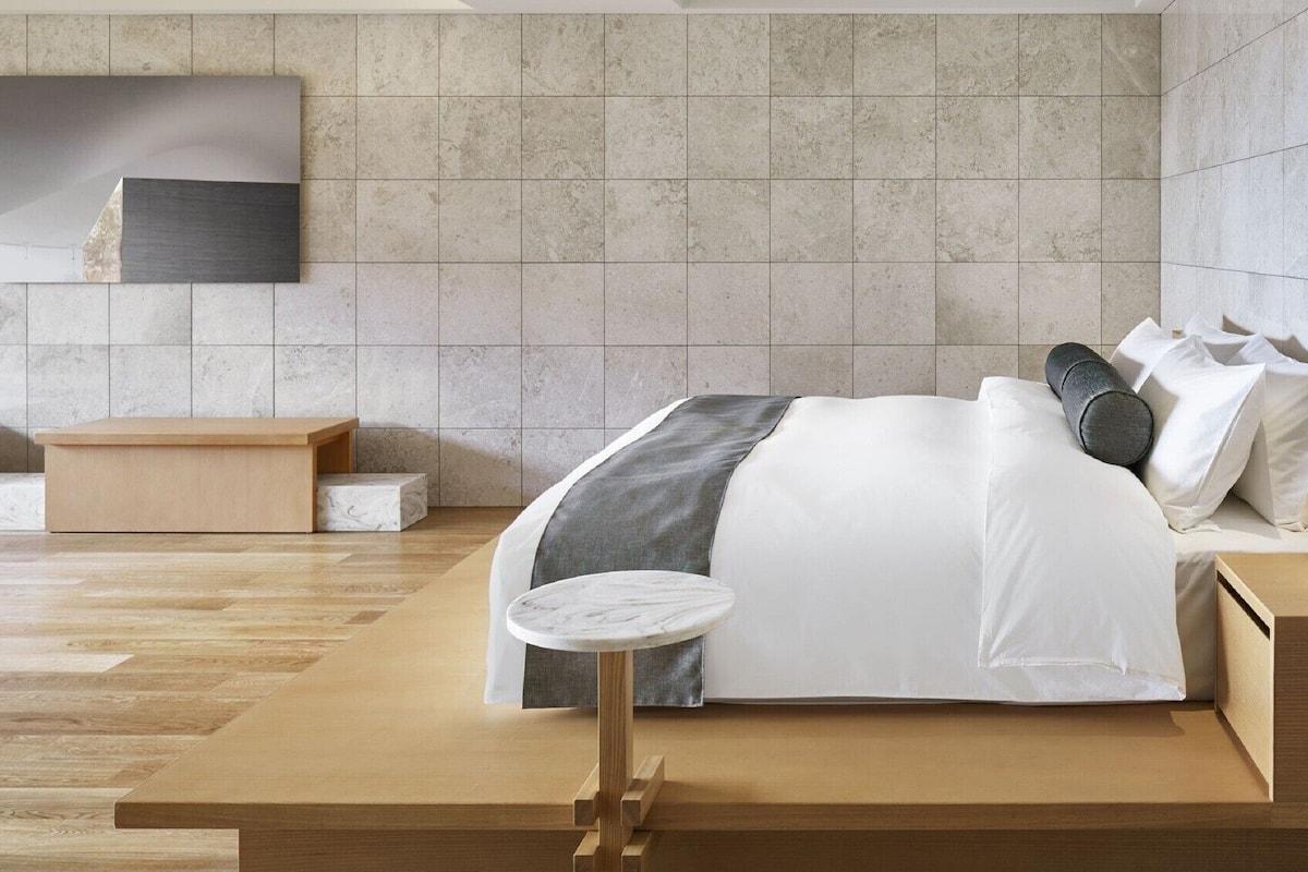 Un dormitorio moderno con una cama grande, una mesita redonda pequeña y un banco.