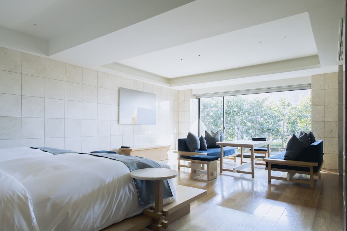 Una habitación de hotel moderna con una cama grande, una mesita pequeña redonda y una zona de estar con sofás y cojines.