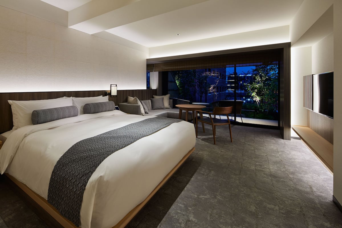 Una habitación de hotel moderna con una cama grande, un escritorio y vistas de la ciudad de noche.