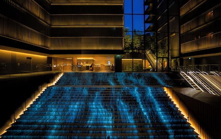 A modern building with a central staircase illuminated by blue lights, surrounded by glass railings and a pool.