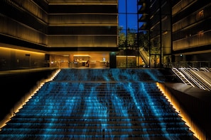 A modern building with a central staircase illuminated by blue lights, surrounded by glass railings and a pool. - THE THOUSAND KYOTO (Kyoto)