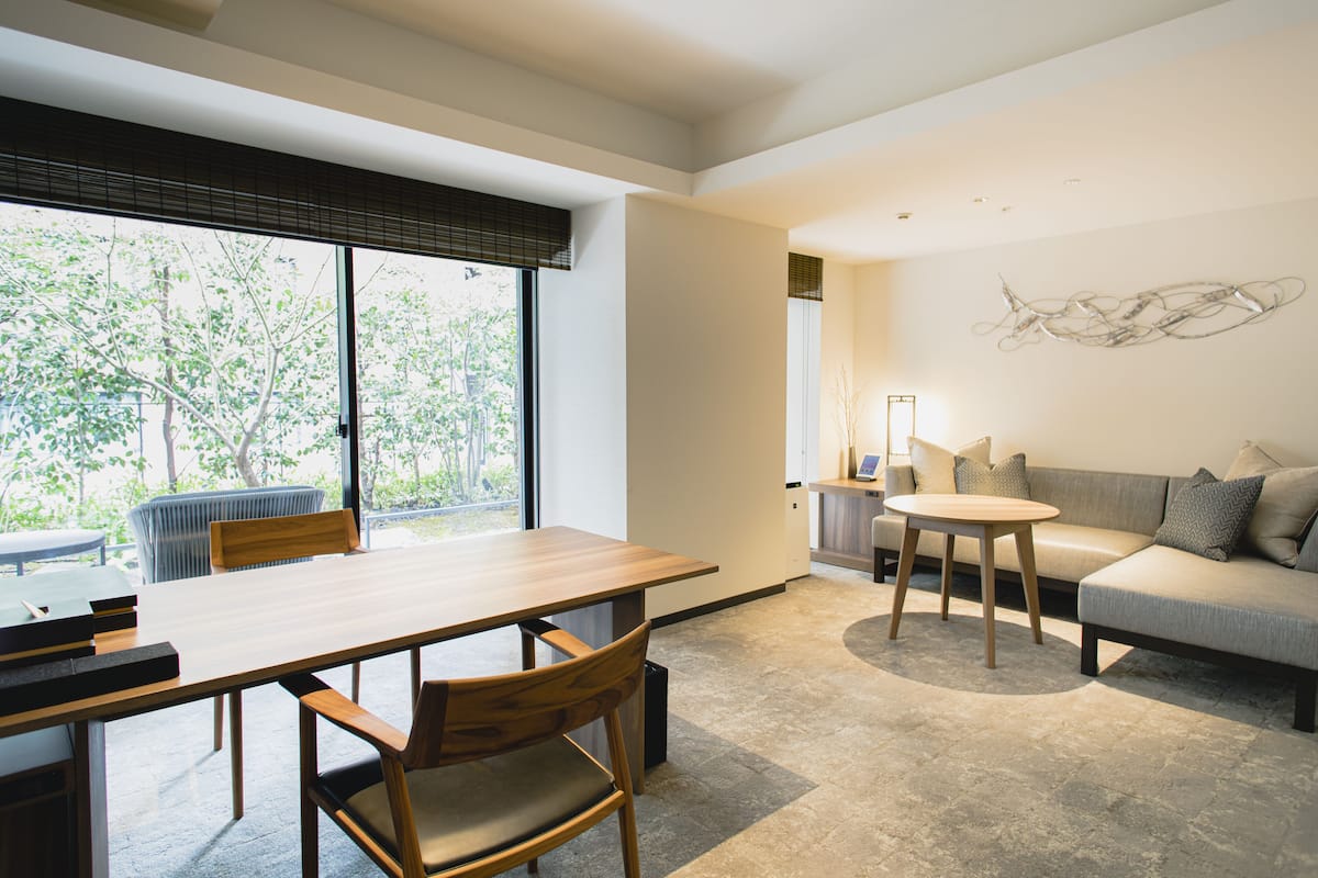 Una sala de estar moderna con una mesa de comedor de madera, un sofá y un ventanal con persianas.