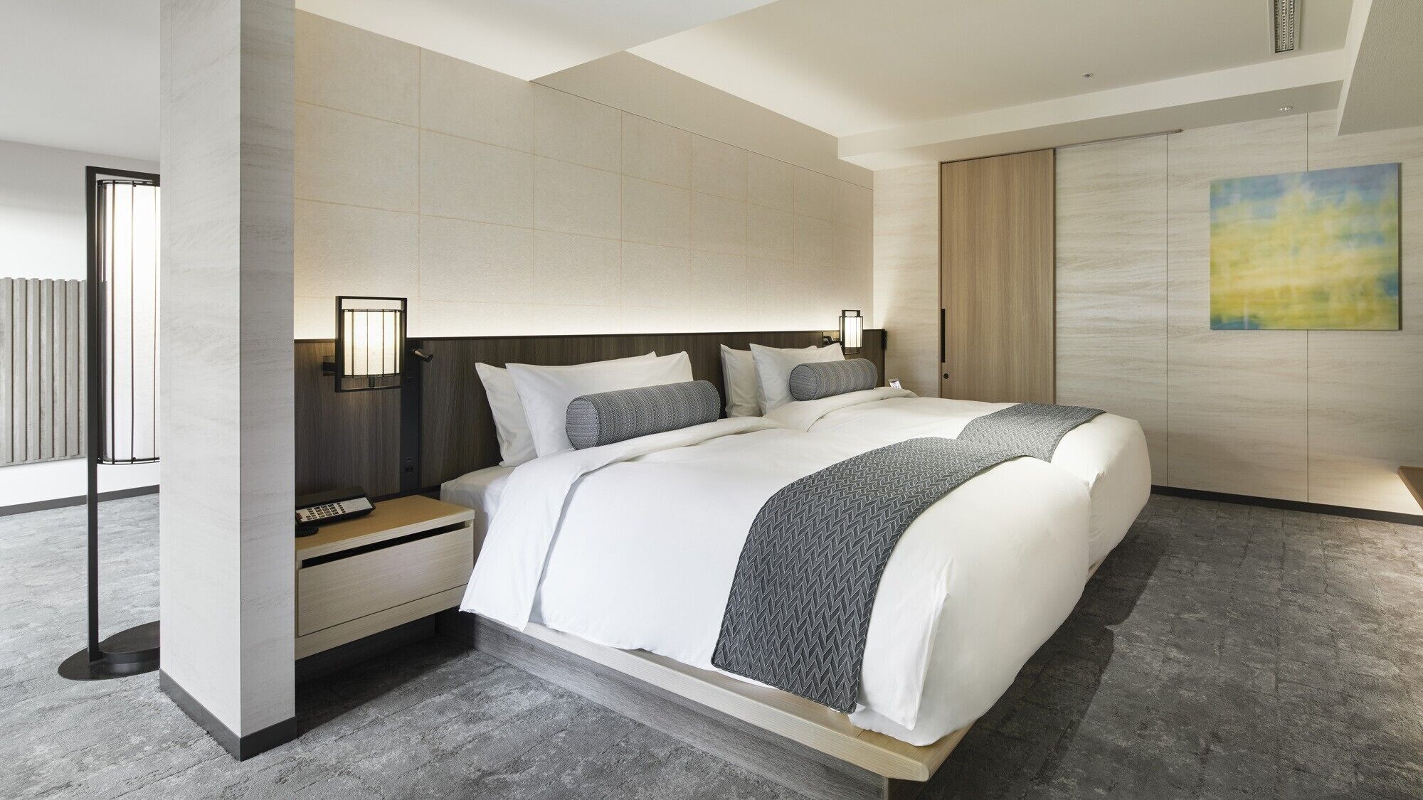 Ein modernes Hotelzimmer mit einem großen Bett, einem Nachttisch, einer Wandlampe und einem Gemälde an der Wand.
