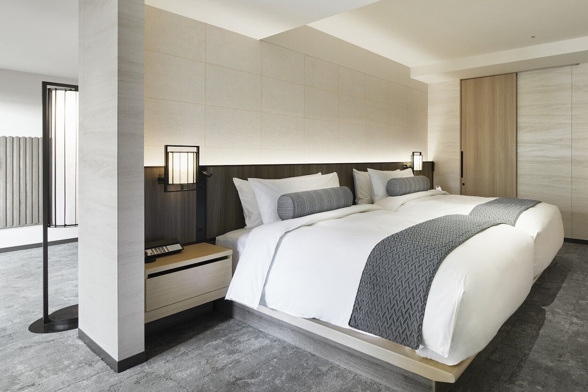 Una habitación de hotel moderna con una cama grande, una mesita de noche, una lámpara de pared y un cuadro en la pared.