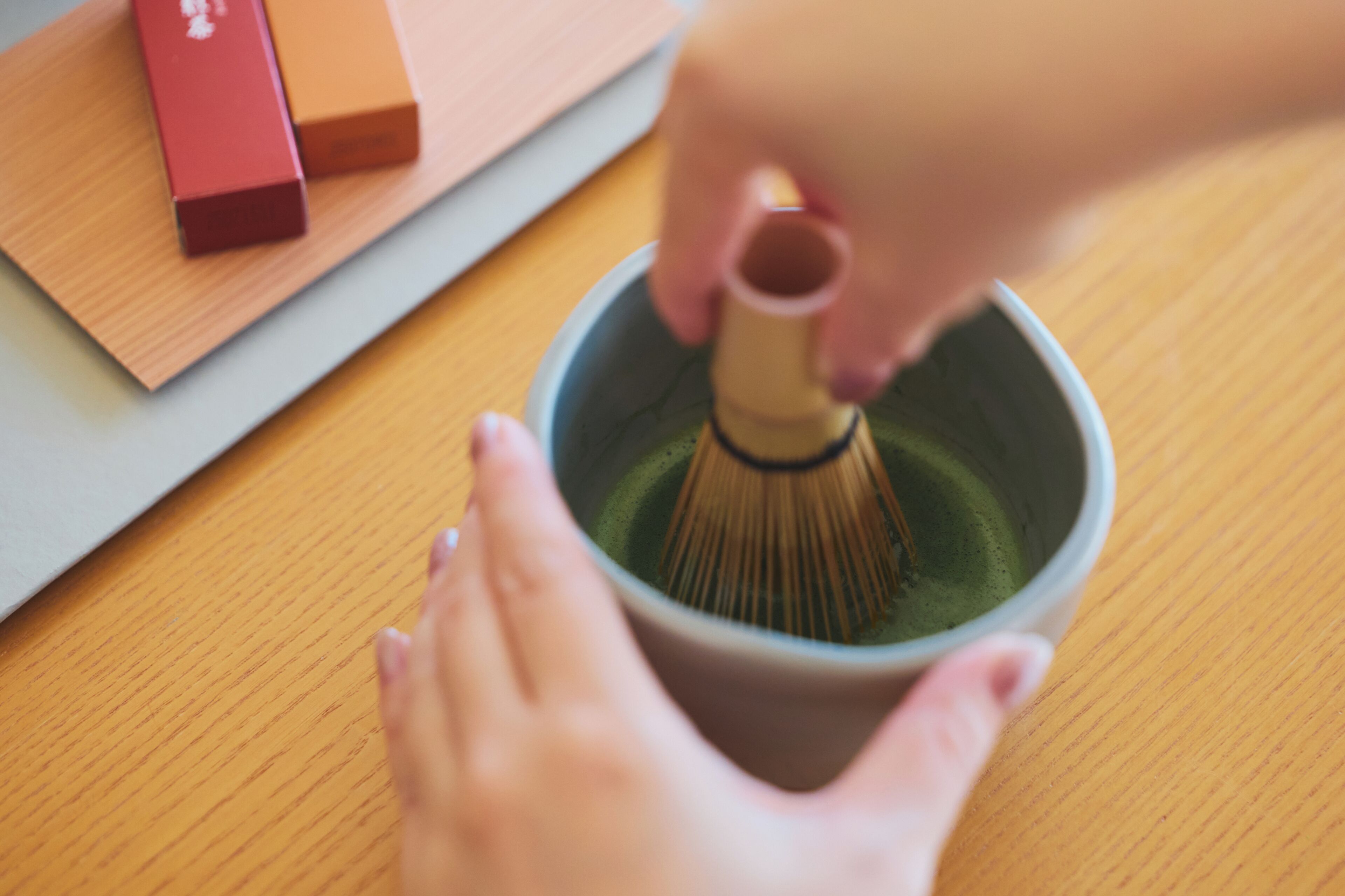 A person whisking matcha in a cup on a wooden table.