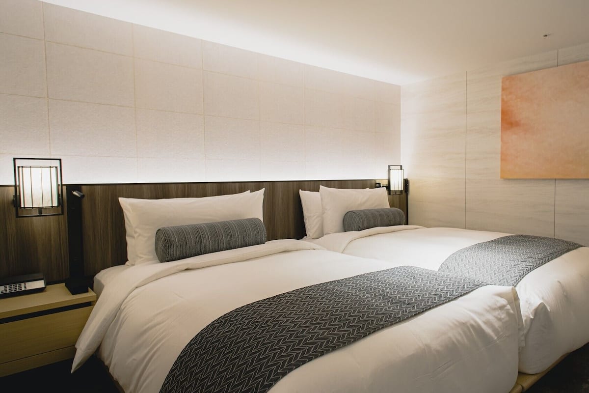 Una habitación de hotel con una cama grande, una mesita de noche, una lámpara de pared y un cuadro.