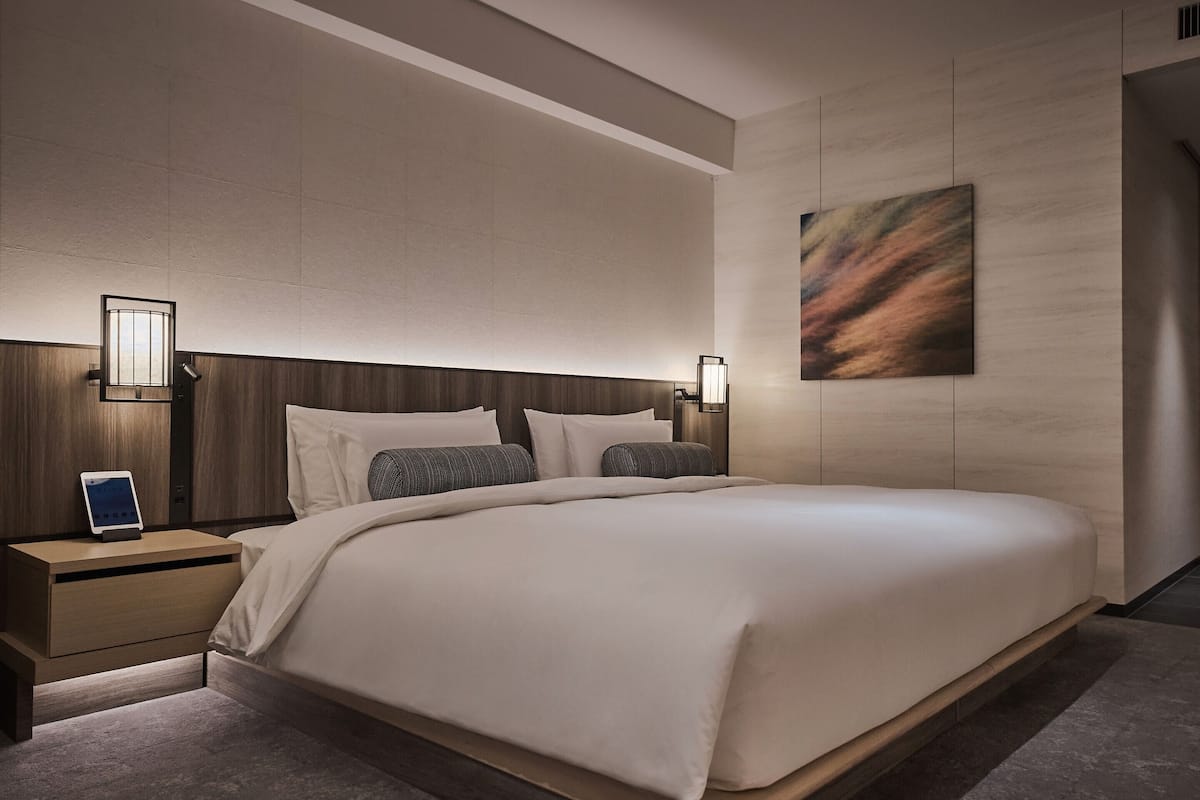 Una habitación de hotel moderna con una cama grande, mesitas de noche, una lámpara de pared y un cuadro.