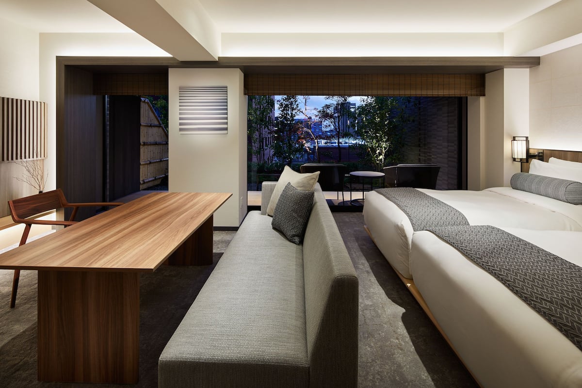Una habitación de hotel moderna con una mesa de comedor de madera, un sofá, una cama y una mesita redonda.
