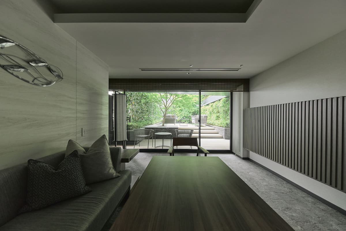 Un interior moderno con un sofá, una mesa de madera y vistas a un patio exterior.