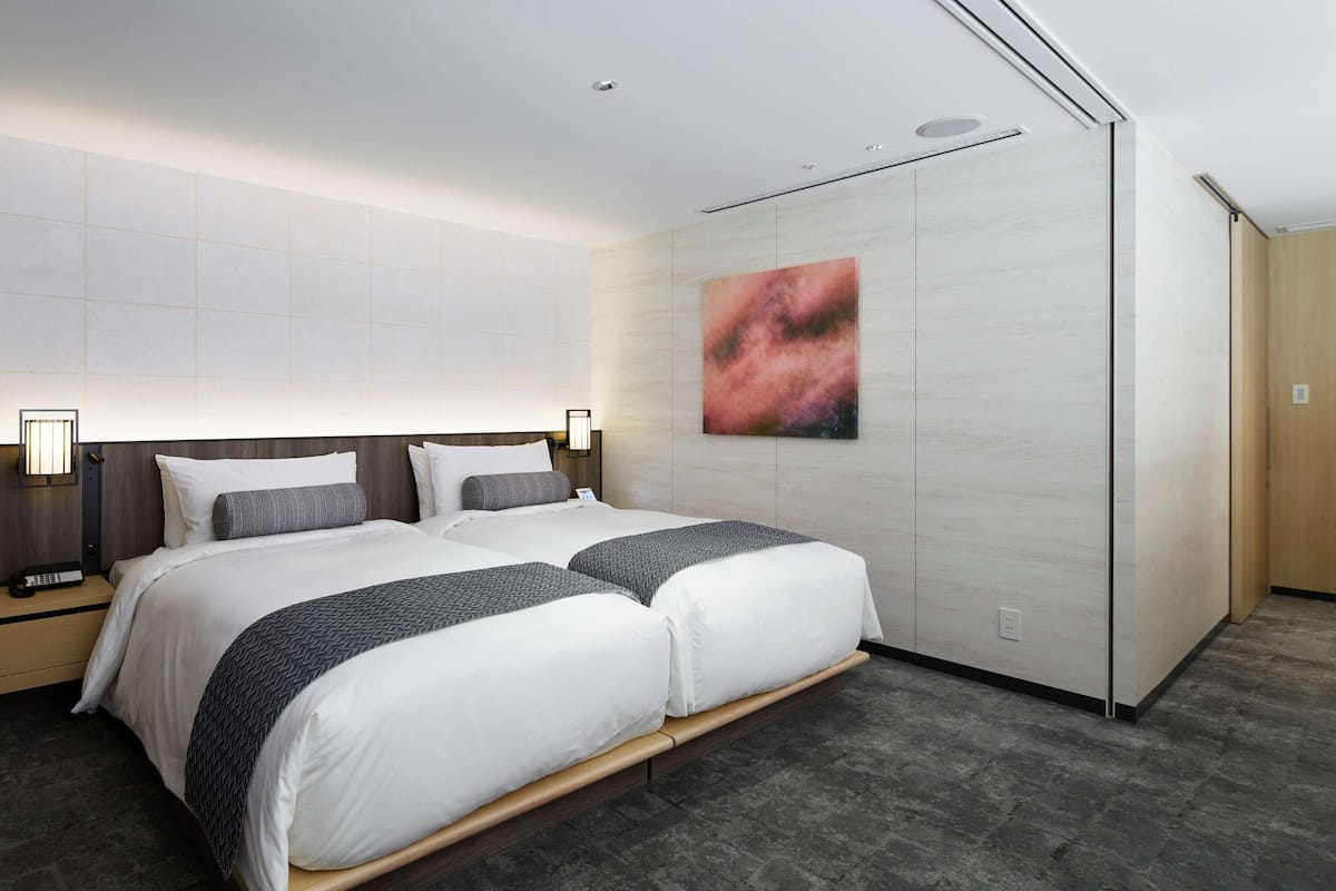 Una habitación de hotel moderna con una cama grande, dos mesitas de noche, una lámpara de pared y un cuadro.