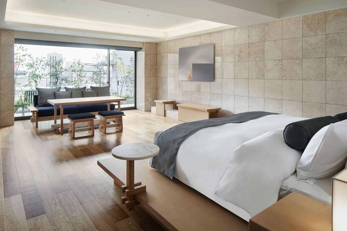 Un dormitorio moderno con una cama grande, una mesita redonda, un sofá y un comedor con vistas a la ciudad.