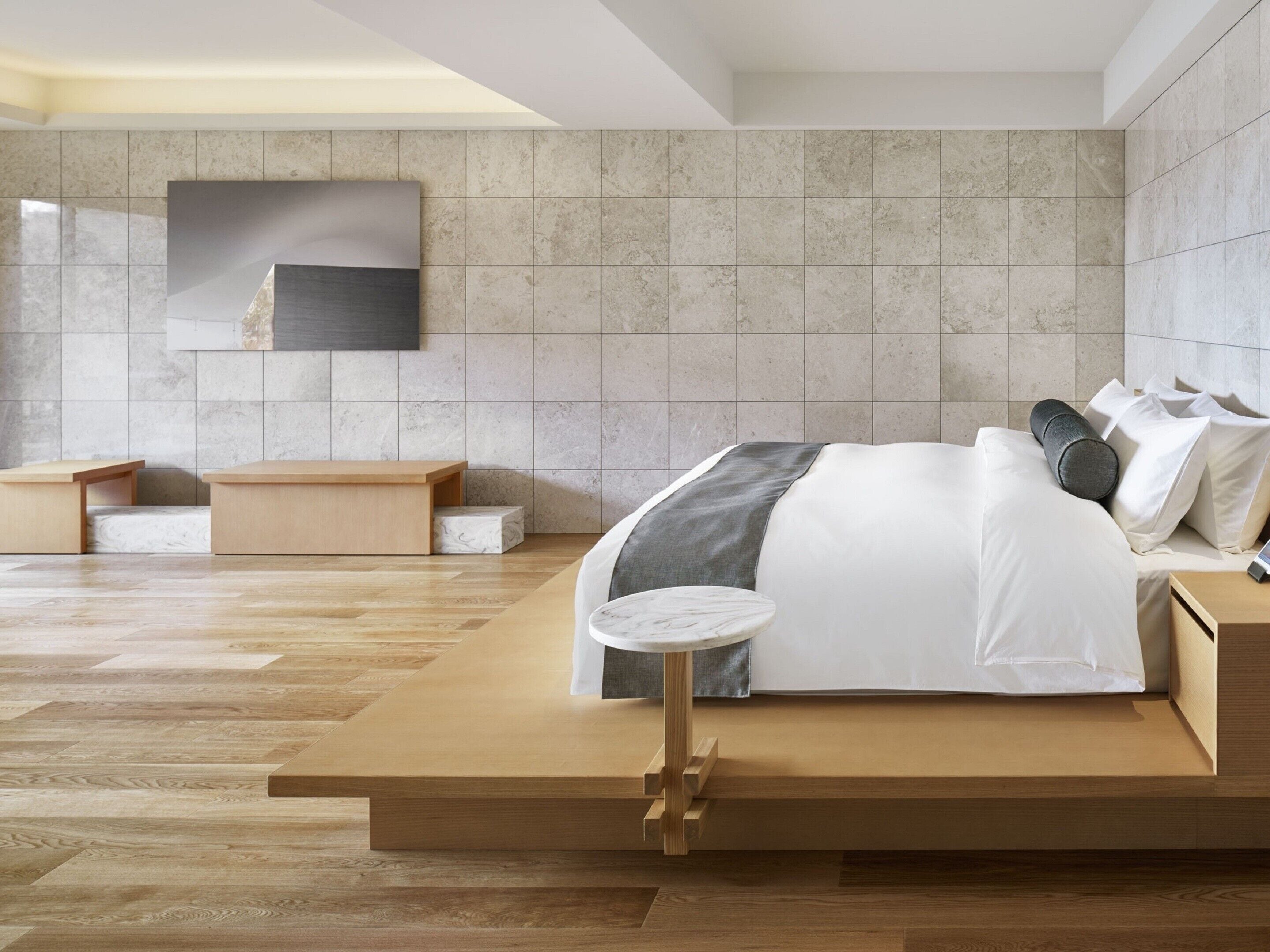 A modern bedroom with a large bed, wooden nightstands, a small round table, and a large wall-mounted TV.