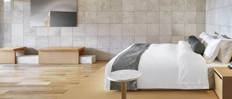 A modern bedroom with a large bed, wooden nightstands, a small round table, and a large wall-mounted TV.