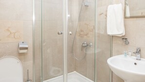 Un baño moderno con ducha envuelta en vidrio, un lavamanos blanco y un inodoro.