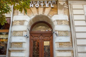 A hotel entrance with a sign above the door, a number plaque on the wall, and a decorative metal gate.